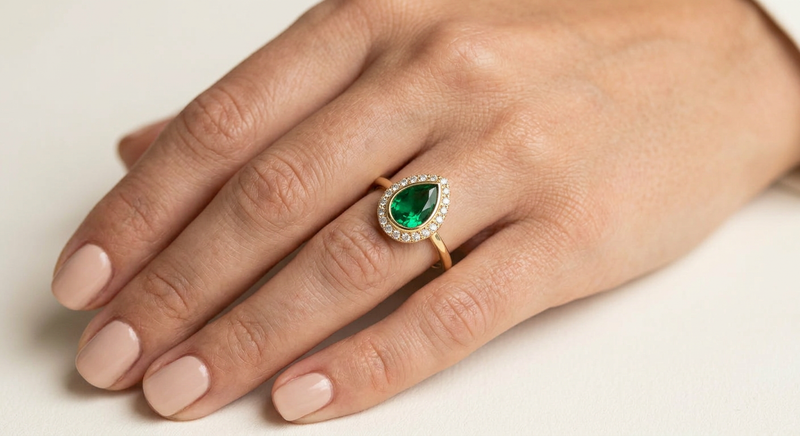 Bague Ocelle portée à l'annulaire — émeraude taille poire et halo de diamants, or jaune — Carron Olivier