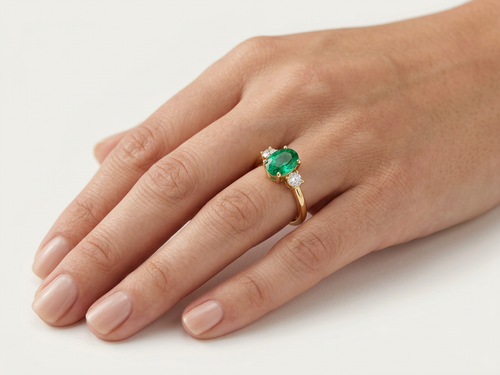 Bague Trilogie portée à l'annulaire — émeraude ovale et deux diamants, or jaune — Carron Olivier