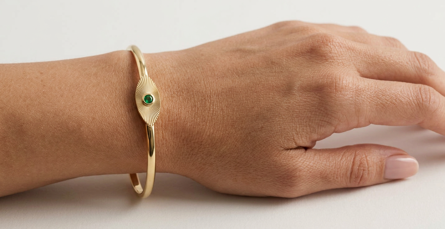 Bracelet Ocelle porté au poignet — jonc en or jaune, plaque gravée et émeraude — Carron Olivier